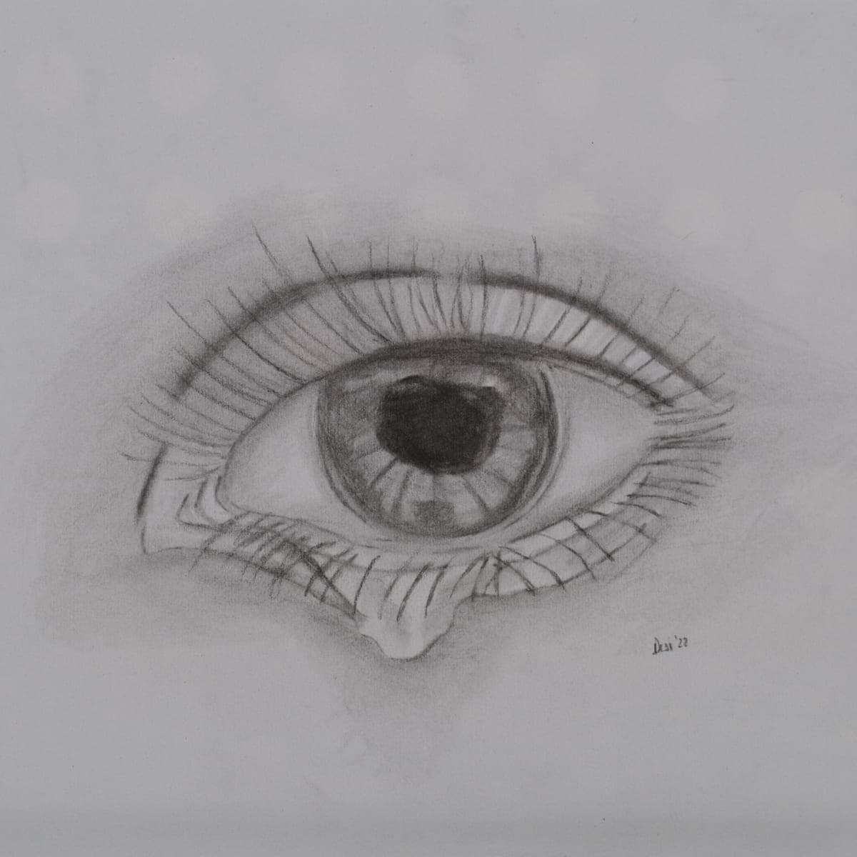 A large charcoal drawing of an eye with a tear