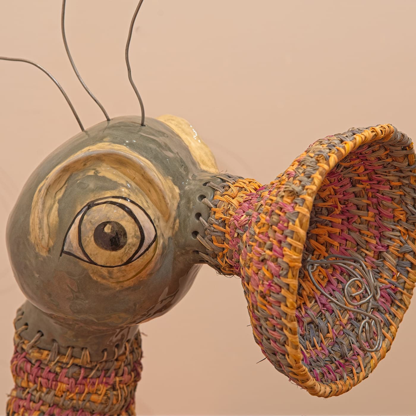A hand-built clay head with a single painted eye, joined to a large woven horn