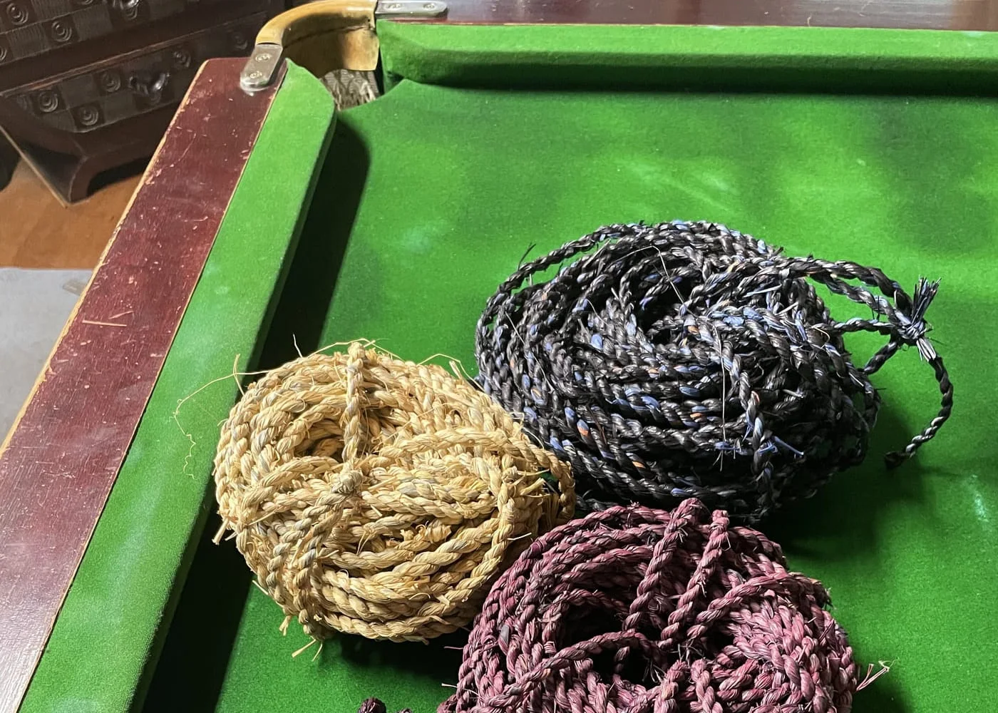 Three coils of braided cord in natural straw, charcoal and plum on a green baize table