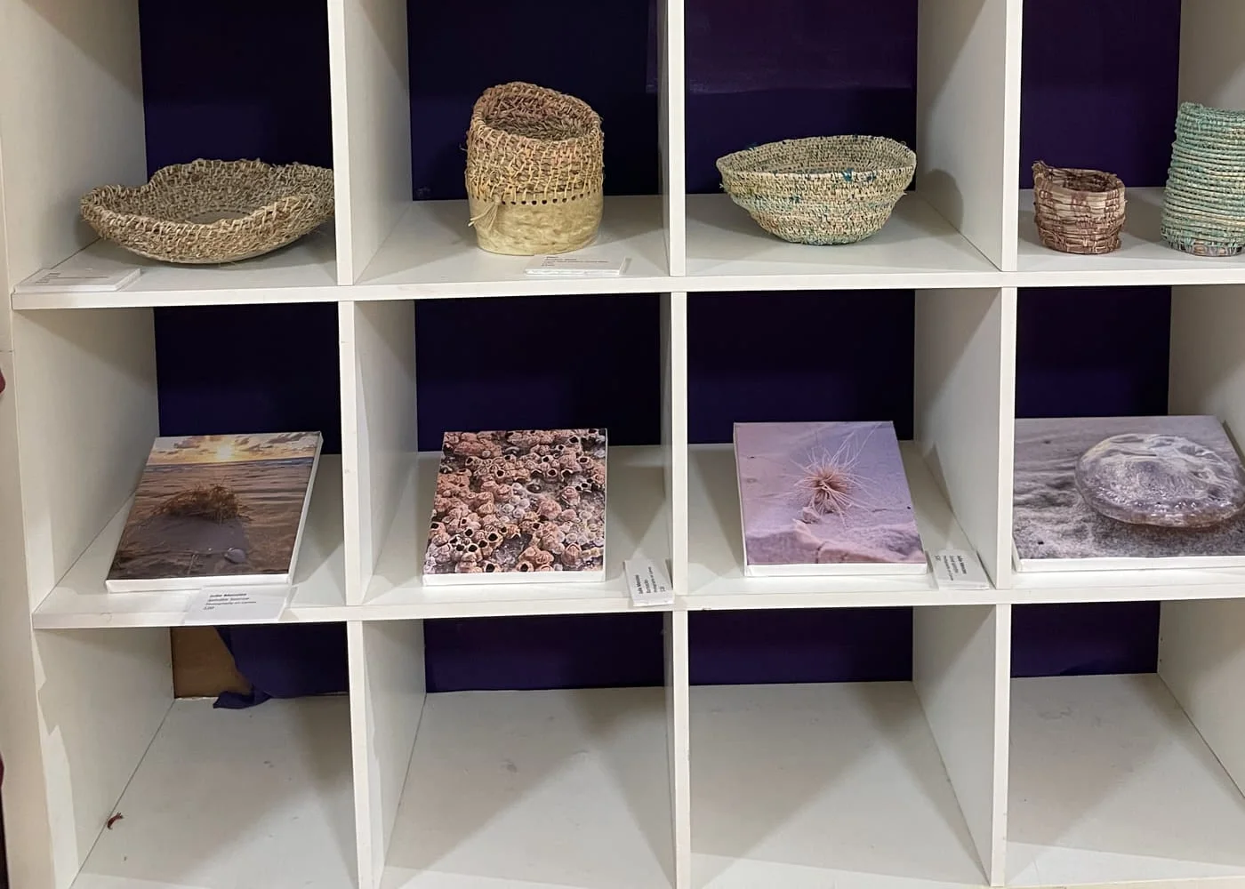 White cube shelving with small woven baskets on top and mounted prints below