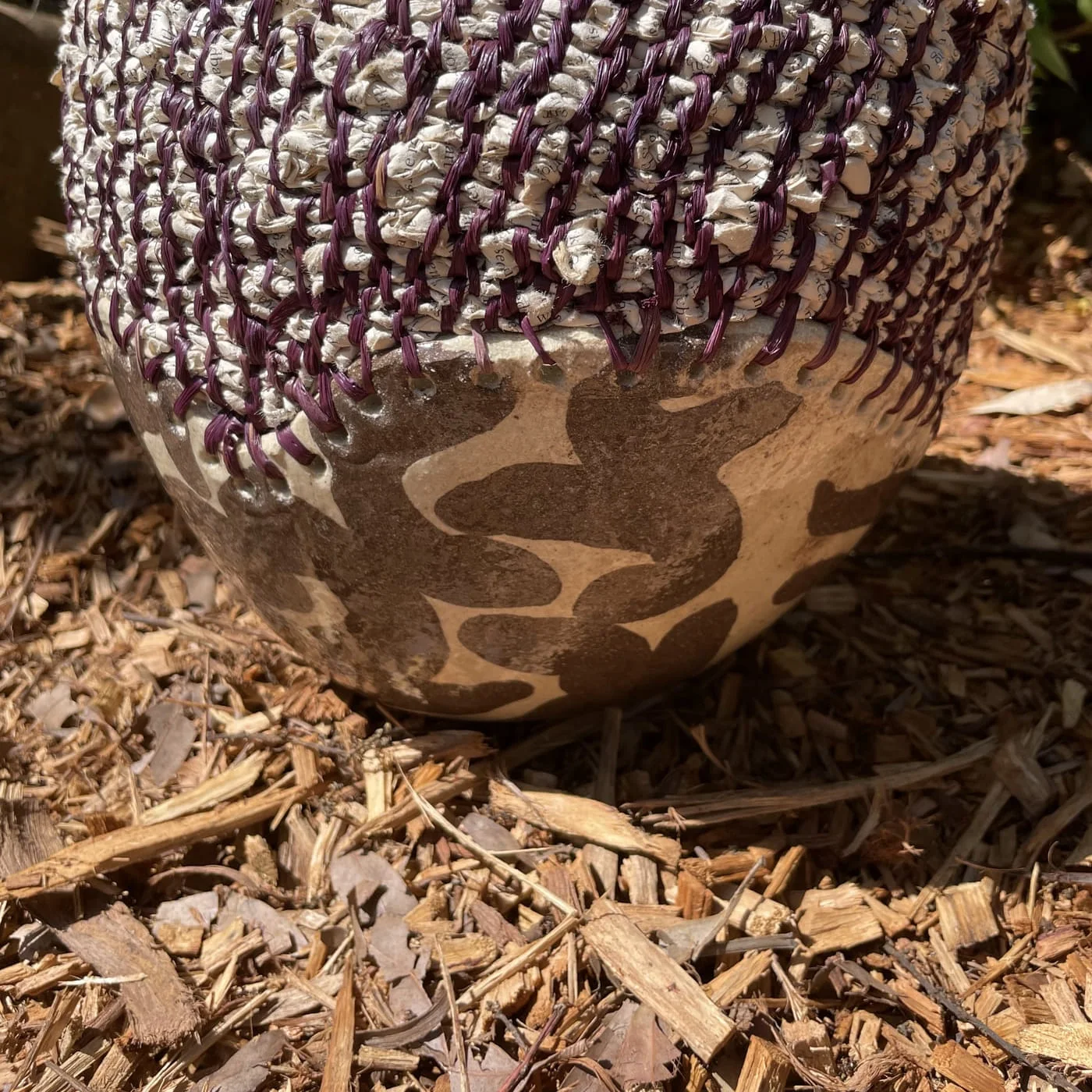 Plum and cream coiled fibre above a mottled clay base, resting on bark mulch