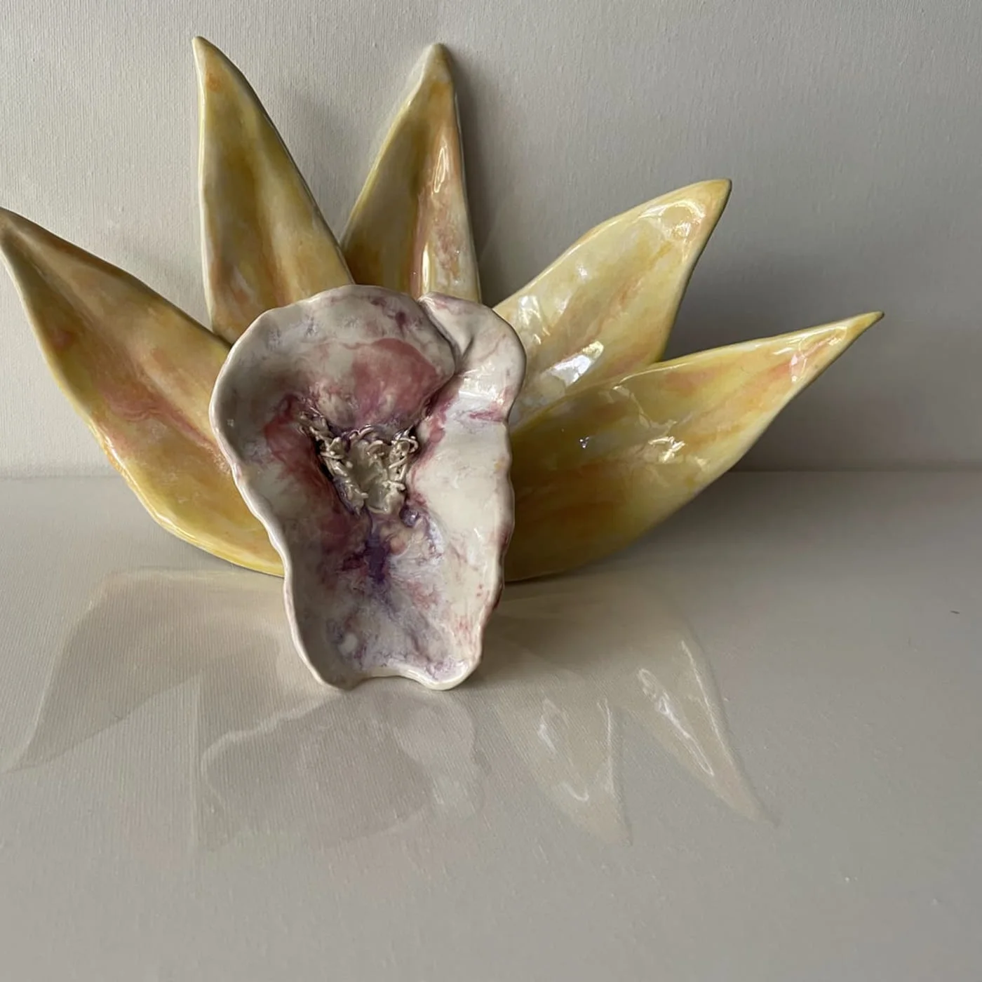 A ceramic flower with pale yellow-green pointed petals around a ruffled violet centre, on white