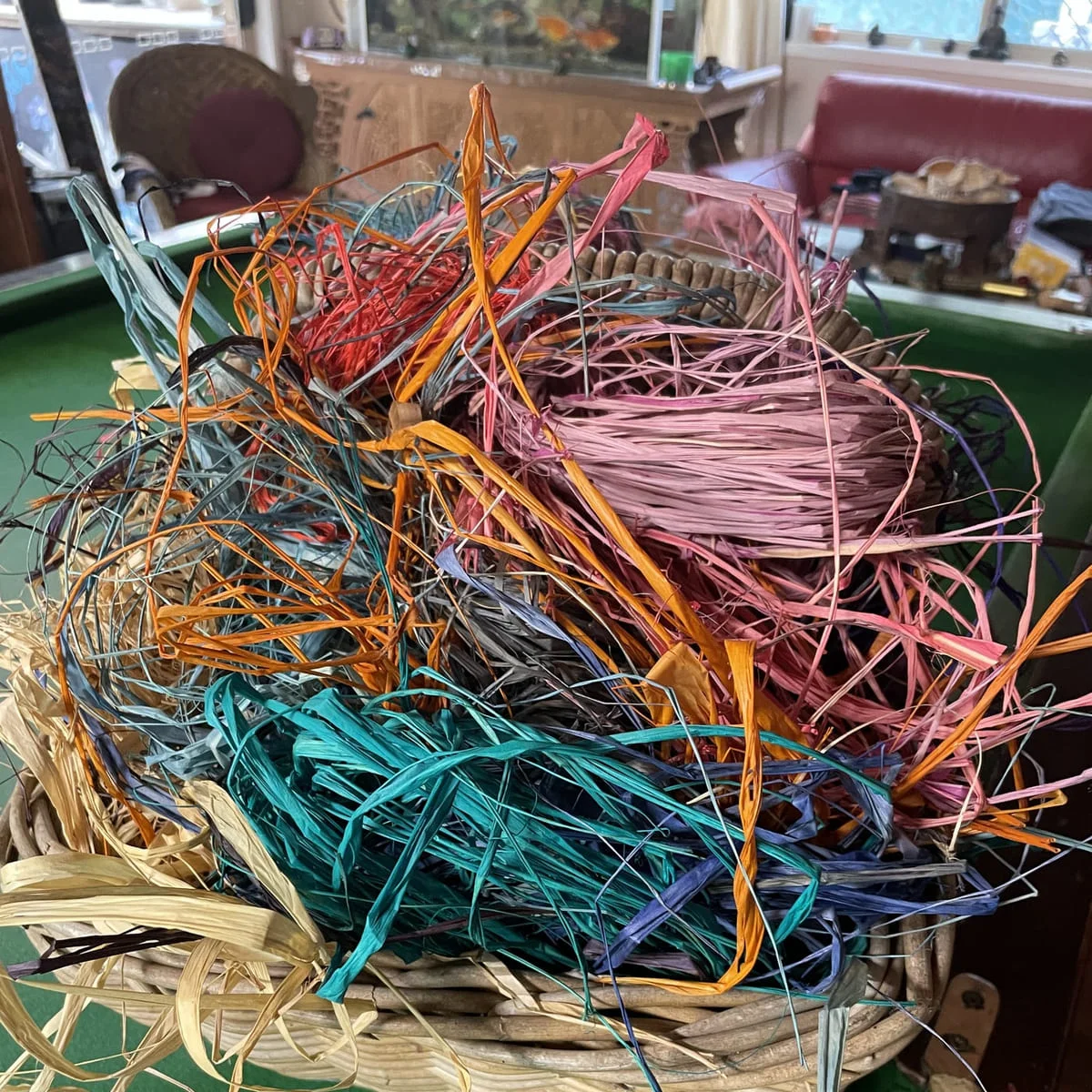 A basket overflowing with raffia offcuts in teal, orange, pink and natural
