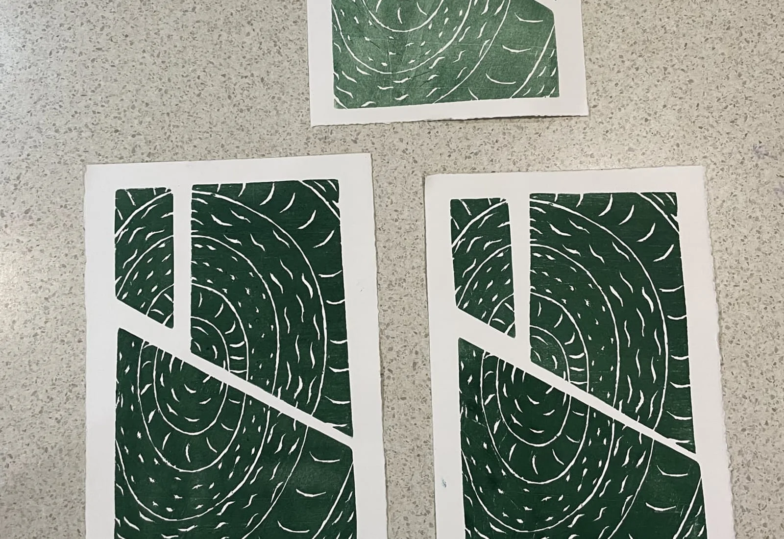 Three green relief prints of a spiral pattern on a speckled bench