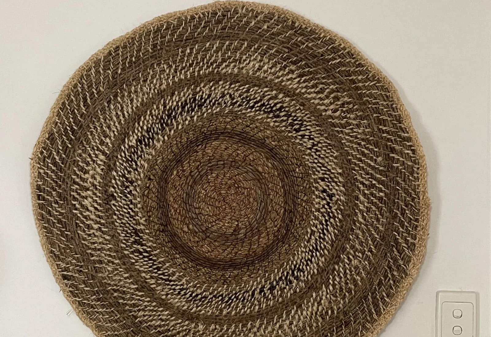 A large, flat coiled mat hung on a white wall